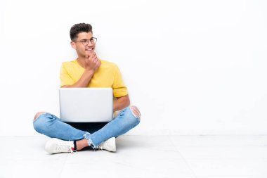 Genç adam beyaz arka planda izole bir şekilde yerde oturuyor.