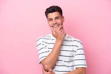 Pembe arka planda izole edilmiş genç beyaz adam mutlu ve gülümsüyor.