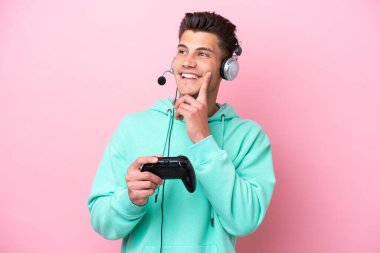 Pembe arka planda izole edilmiş bir bilgisayar oyunu kontrolörüyle oynayan yakışıklı beyaz bir adam yukarı bakarken bir fikir düşünüyor.