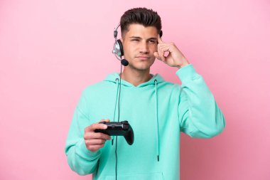 Pembe arka planda izole edilmiş bir bilgisayar oyunu kontrolörüyle oynayan yakışıklı beyaz bir adamın şüpheleri ve düşünceleri var.