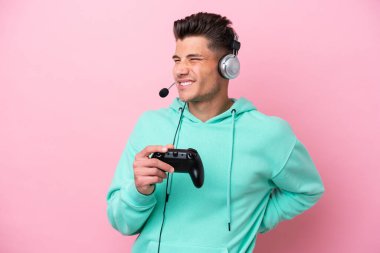 Pembe arka planda izole edilmiş bilgisayar oyunu kontrolörüyle oynayan yakışıklı beyaz bir adam gayret gösterdiği için sırt ağrısından muzdarip.