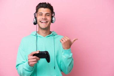 Pembe arka planda izole edilmiş bir bilgisayar oyunu kontrolörüyle oynayan yakışıklı beyaz bir adam bir ürünü sunmak için kenarı işaret ediyor.