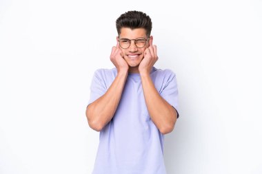 Beyaz arka planda izole edilmiş genç beyaz adam hayal kırıklığına uğramış ve kulaklarını kapatmış.