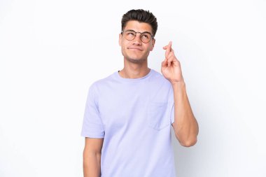 Beyaz arka planda izole olmuş genç beyaz bir adam parmaklarını çapraz yapıp en iyisini diliyor.
