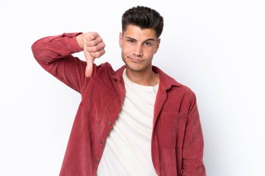 Beyaz arka planda izole genç beyaz adam olumsuz ifade ile baş parmağını göstermektedir