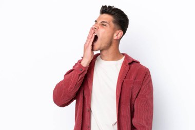 Beyaz arka planda izole edilmiş genç beyaz bir adam esniyor ve geniş bir ağzı eliyle kapatıyor.