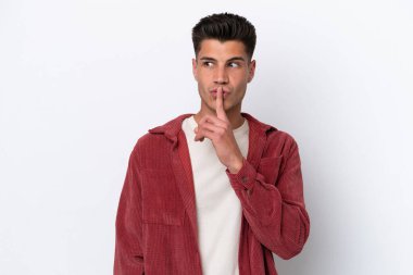 Beyaz arka planda izole edilmiş genç beyaz bir adam sessizlik işareti gösteriyor. Parmağını ağzına sokuyor.