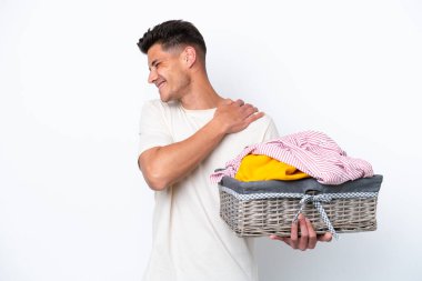 Çamaşır sepetini tutan beyaz arka planda omuz ağrısı çeken genç beyaz bir adam var.