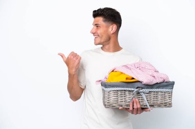 Young caucasian man holding laundry basket isolated on white background pointing to the side to present a product