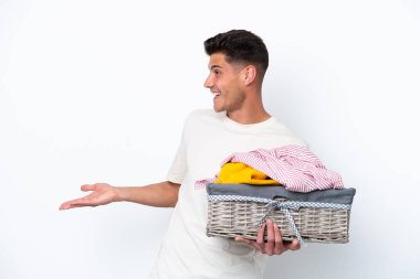 Beyaz arka planda çamaşır sepetini tutan beyaz tenli genç bir adam.