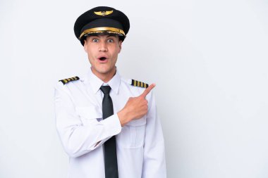 Beyaz arka planda izole edilmiş Kafkasyalı uçak pilotu şaşırmış ve işaret ediyor.