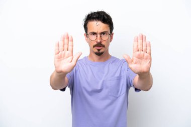 Bıyıklı genç adam beyaz arka planda izole edilmiş. Durma hareketi yapıyor ve hayal kırıklığına uğruyor.