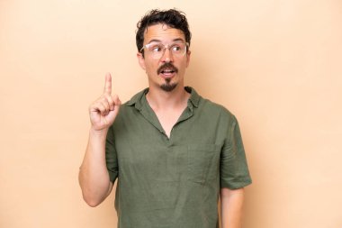 Beyaz tenli genç adam bej arka planda izole edildi. Çözümü bulmak için parmağını kaldırdı.