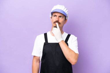 Mor arka planda izole edilmiş önlük giyen balıkçı adamın yukarı bakarken şüpheleri var.