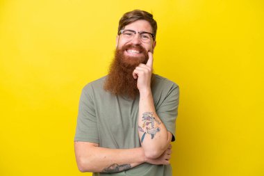 Sarı arka planda sakallı kızıl saçlı adam gülüyor.