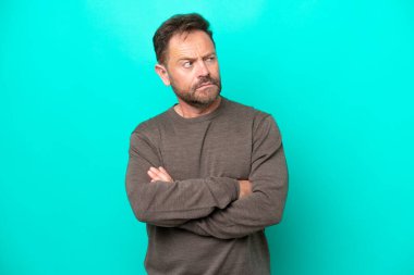 Mavi arka planda izole edilmiş orta yaşlı beyaz bir adam şüpheli hareketler yapıyor.