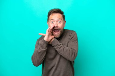 Mavi arka planda izole edilmiş orta yaşlı beyaz bir adam bir ürün sunmak ve bir şeyler fısıldamak için kenarı işaret ediyor.