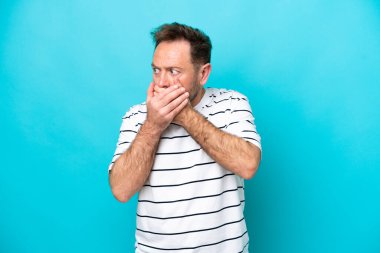 Orta yaşlı, beyaz bir adam mavi arka planda izole edilmiş, ağzı kapalı ve yana bakıyor.