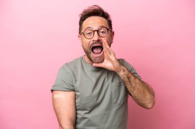 Pembe arka planda izole edilmiş yara bandı takan orta yaşlı bir adam ağzı açık bağırıyor.