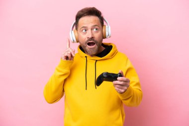 Orta yaşlı bir adam pembe arka planda izole edilmiş bir bilgisayar oyunu kontrolörüyle oynuyor.