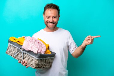 Mavi arka planda izole edilmiş çamaşır sepetini tutan orta yaşlı bir kadın var.