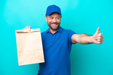 Orta yaşlı bir adam mavi arka planda izole edilmiş bir paket yiyecek alıyor.