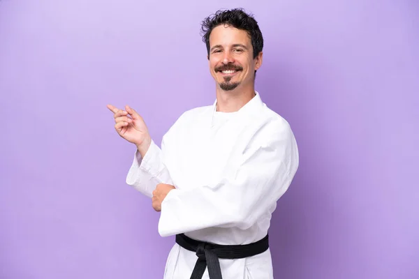 Mladý Běloch Dělá Karate Izolované Fialovém Pozadí Ukazující Prstem Stranu — Stock fotografie
