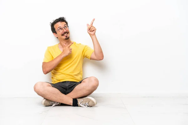 Joven Hombre Caucásico Sentado Suelo Aislado Sobre Fondo Blanco Señalando — Foto de Stock