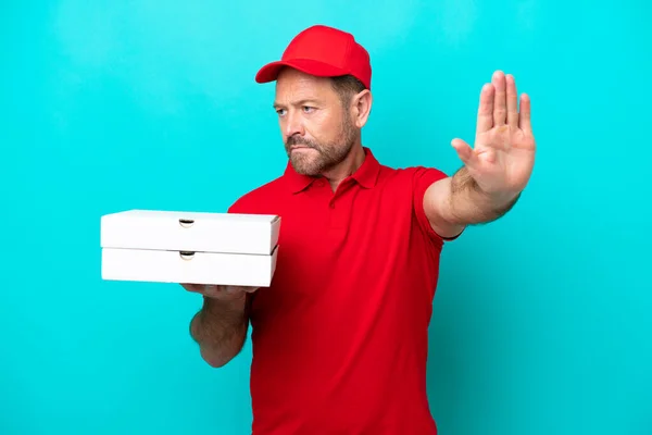 Pizza delivery man with work uniform picking up pizza boxes isolated on blue background making stop gesture and disappointed