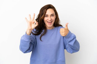 Beyaz arka planda izole edilmiş genç beyaz bir kadın tamam işareti ve baş parmak hareketi gösteriyor.