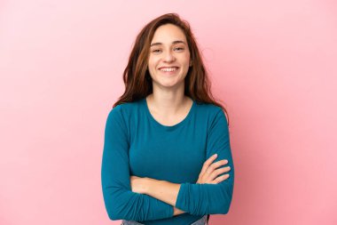 Pembe arka planda izole edilmiş genç beyaz kadın kollarını ön cephede çapraz tutuyor.