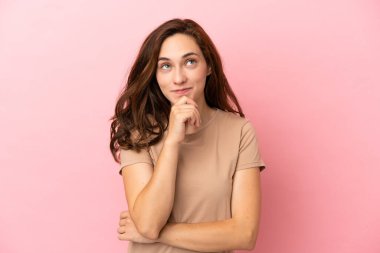 Pembe arka planda izole edilmiş genç beyaz kadın yukarı bakarken bir fikir düşünüyor.