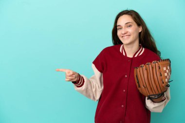 Beyzbol oynayan beyaz bir kadın. Mavi arka planda izole edilmiş. Parmağını kenarı işaret ediyor.