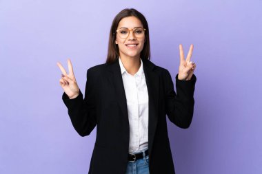 Mor arka planda izole edilmiş bir iş kadını zafer işaretini iki eliyle gösteriyor.