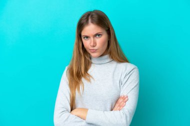 Genç sarışın kadın mutsuz bir ifadeyle mavi arka planda izole edilmiş.