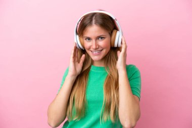 Pembe arka planda izole edilmiş genç sarışın kadın müzik dinliyor.