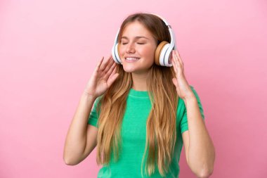 Genç sarışın kadın pembe arka planda izole edilmiş müzik dinliyor ve şarkı söylüyor.