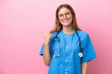 Pembe arka planda izole edilmiş genç cerrah kadın bir ürünü sunmak için kenarı işaret ediyor.