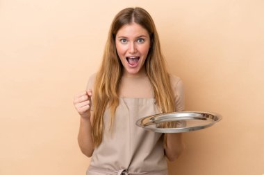 Bej arka planda tepsisi olan genç sarışın garson kadın galibiyeti kutluyor.