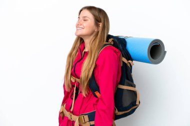 Büyük bir sırt çantasıyla izole edilmiş beyaz bir arka planı olan dağcı kız yan pozisyonda gülüyor.