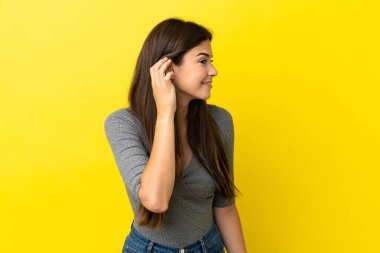 Sarı arka planda izole edilmiş genç Brezilyalı bir kadın. Kulağına elini sürerek bir şeyler dinliyor.