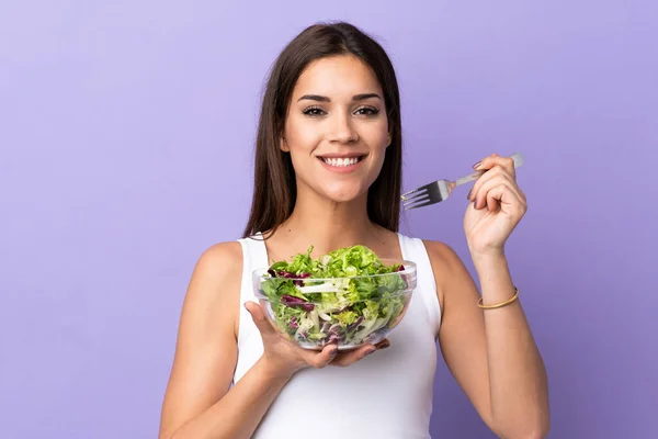 Young caucasian woman with salad isolated on purple background