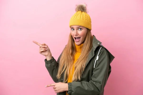 Jovem Loira Usando Casaco Inverno Isolado Fundo Rosa Surpreso Apontando — Fotografia de Stock