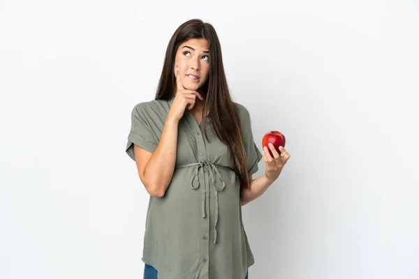 白い背景に孤立した若いブラジル人女性妊娠中のリンゴを保持しながら考える — ストック写真