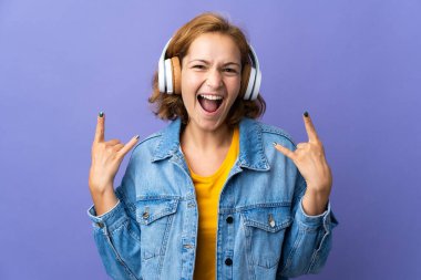 Genç Gürcü kadın mor arka planda izole edilmiş rock hareketlerini dinlerken müzik dinliyor.