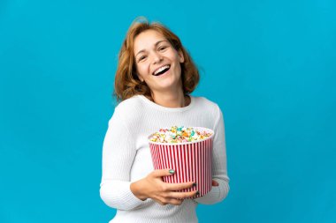 Genç Gürcü bir kadın mavi arka planda izole edilmiş. Elinde koca bir kova patlamış mısır var.