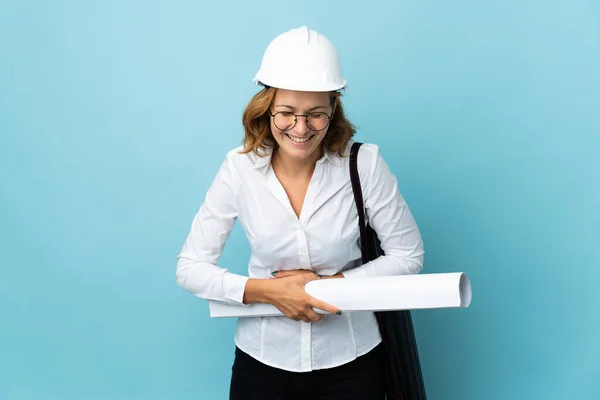 Young architect Georgian woman with helmet and holding blueprints over isolated background smiling a lot