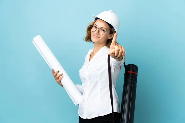 Young architect Georgian woman with helmet and holding blueprints over isolated background showing and lifting a finger