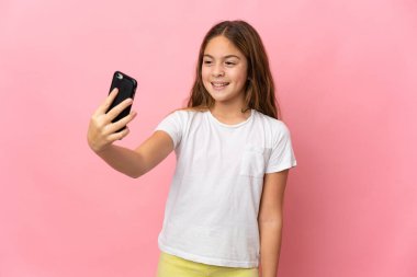 İzole edilmiş pembe arka planı olan çocuk cep telefonuyla selfie çekiyor.