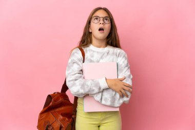 İzole edilmiş pembe arka planda küçük öğrenci kız yukarı bakıyor ve şaşırmış bir ifadeyle